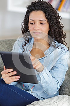 Woman lying on sofa at home using digital tablet