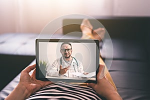 Woman lying on a sofa and talking with a doctor online using digital tablet. Telemedicine concept.