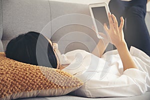 Woman lying on the sofa using mobile phone to work at home. Asian Female holding phone and touch screen via tablet. Technology