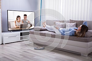 Woman Lying On Sofa Watching Television