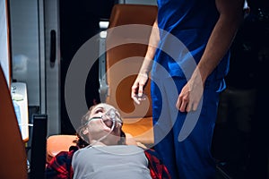 A woman lying on a stretcher with an oxigen mask on and looking at the paramedic in a blue uniform