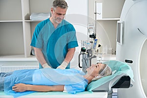 Woman is lying on table tomograph, doctor is standing next to her