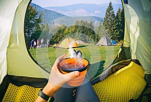 Woman lying in a tent with coffee ,view of camping