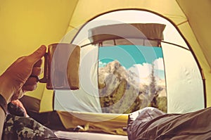 Woman lying in a tent with coffee ,view of mountains and sky