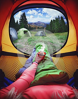 Woman lying in a tent with coffee ,view of mountains and sky