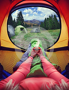 Woman lying in a tent with coffee ,view of mountains and sky