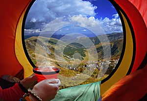 Woman lying in a tent with coffee ,view of mountains and sky