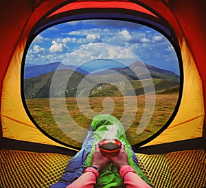 Woman lying in a tent with coffee ,view of mountains and sky