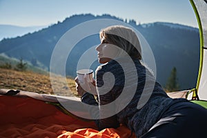 Woman lying in tent and looking mountain landscape.