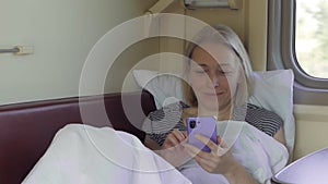 A woman lying in a train compartment using the Internet in a smartphone during a trip