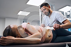 Woman lying on treatment bed physiotherapist presses her abs with IASTM instrument side view photo