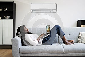 Woman Lying Under Air Conditioner On Couch Using Laptop