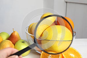 Woman with magnifying glass exploring lemons indoors, closeup. Poison detection
