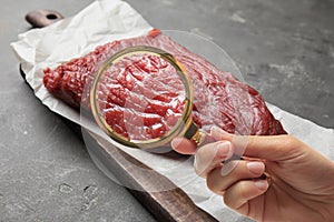 Woman with magnifying glass focusing on fresh raw meat, closeup. Food control