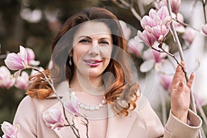 Woman magnolia flowers, surrounded by blossoming trees., hair down, wearing a light coat. Captured during spring