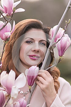 Woman magnolia flowers, surrounded by blossoming trees., hair down, wearing a light coat. Captured during spring