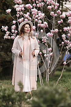 Woman magnolia flowers, surrounded by blossoming trees., hair down, white hat, wearing a light coat. Captured during