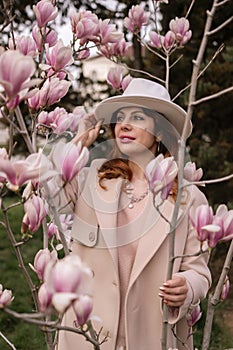 Woman magnolia flowers, surrounded by blossoming trees., hair down, white hat, wearing a light coat. Captured during