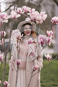 Woman magnolia flowers, surrounded by blossoming trees., hair down, white hat, wearing a light coat. Captured during