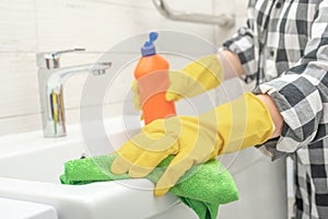 Woman maid or charwoman cleaning sink in bathroom, cleaning bathroom at home. Cropped view of woman in rubber gloves wet rag and