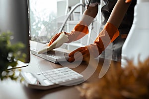 Woman maid cleaning and wiping the keyboard with microfiber cloth at desk in office