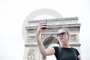 Woman make selfie with phone at arc de triomphe in paris, france. Woman with smartphone at arch monument. Vacation and sightseeing