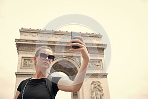 Woman make selfie with phone at arc de triomphe in paris, france. Woman with smartphone at arch monument. Vacation and