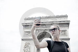 Woman make selfie with phone at arc de triomphe in paris, france. Woman with smartphone at arch monument. Vacation and