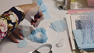 A woman makes a greeting card. Glues paper elements in the shape of a rose. Tools and materials are laid out nearby