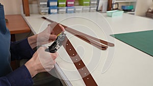 A woman makes holes in a leather belt. Leatherworker's workshop.