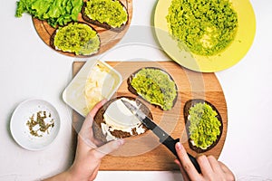 Woman makes a homemade avocado sandwich. White table with a plate of mashed avocado, spices, and a box of cream cheese. Cooking