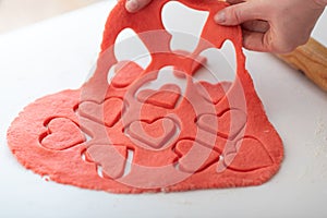 A woman makes homemade Valentine\'s Day cookies from shortcrust pastry in the form of red hearts