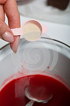 A woman makes jelly from raspberry syrup. Adds a spoonful of agar agar. Levington cake, stages of preparation