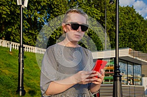 Woman makes shopping on Internet or communicates in instant messengers from smartphone while in park