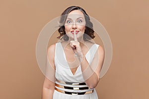 Woman makes silence hush gesture, keeps index fingers over lips, tells secret information to someone