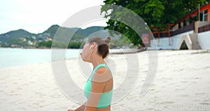 Woman makes warm up exercise on the beach, she sits on yoga mat on the sand