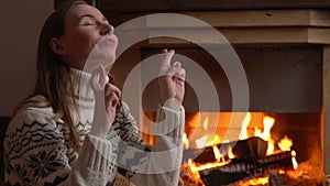 Woman makes a wish to win, raises her hands with crossed fingers, sits near the fireplace