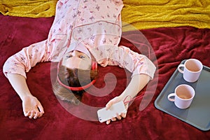 A woman in a makeshift medical mask is isolated during quarantine by the coronavirus. The girl on the bed listens to music from