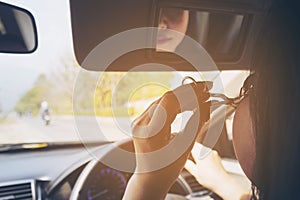 Woman makeup her face using eyelash curler while driving car