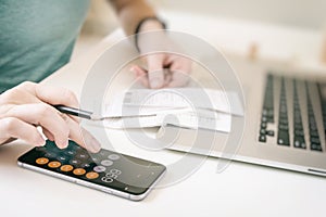 Woman making audit of household spendings at home, using calculator