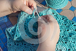 Woman making a blue shawl or scarf with crochet hook in garden at home. hobby or pastime