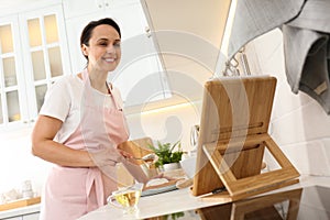 Woman making cake while watching cooking course via tablet in kitchen