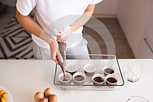 Woman making chocolate muffins at home. Put batter to cupcake forms in glass baking tray on kitchen table close up
