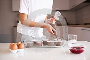 Woman making chocolate muffins at home. Put batter to cupcake forms in glass baking tray on kitchen table close up