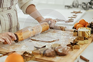 Woman making christmas gingerbread cookies in modern white kitchen close up. Hands kneading gingerbread dough with rolling pin,