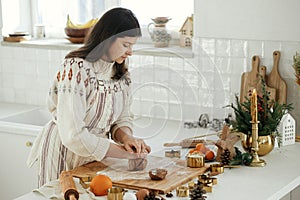 Woman making christmas gingerbread cookies in modern white kitchen. Hand kneading gingerbread dough on wooden board with flour,