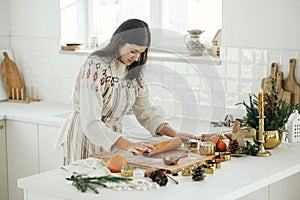 Woman making christmas gingerbread cookies in modern white kitchen. Hand kneading gingerbread dough on wooden board with flour,
