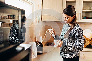 Woman making coffee drink at home kitchen using electric milk frother drink mixer coffee whisk for frothy cream whipped coffee.