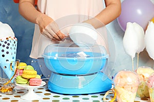 Woman making cotton candy using modern machine at table