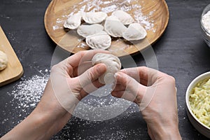 Woman making dumplings (varenyky) at black table, closeup